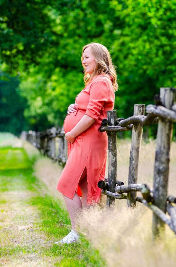 Zwangere vrouw leunend tegen hekwerk